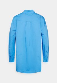 Camisa de manga longa azul clara com corte reto, punhos abotoados, plissado nas costas e gola clássica. Feita de um tecido suave.
