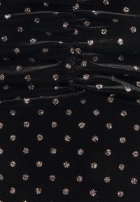 Svart tyg med en rynkig textur, prydd med spridda silvriga glittriga polka prickar i ett konsekvent mönster över ytan.