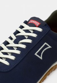 Λευκό κορδόνι σε τζιν μπλε σουέντ αθλητικό παπούτσι, πλαστική ετικέτα με σήμα και ελαστική σόλα από καουτσούκ. Διαθέτει ραμμένο λογότυπο στο πλάι.