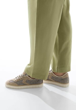 Baskets beiges avec des accents brun texturé, dotées d'une tige en maille et d'une semelle en caoutchouc crème. Portées avec un pantalon ample vert clair.