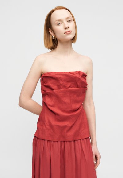 Κόκκινο, στράπλες, υφασμάτινο τοπ με σχεδιασμό από μαζεμένο ύφασμα, συνδυασμένο με μια ασορτί ροή φούστα, δημιουργώντας μια αρμονική εμφάνιση.