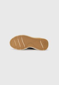 Semelle de chaussure de sport noire avec une surface en caoutchouc texturé, présentant un motif en chevrons et des accents beiges. Bord blanc le long de la semelle.
