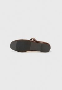 Brown leather shoe with a rounded toe and narrow strap. Textured black sole provides grip. Metallic buckle detail enhances design.