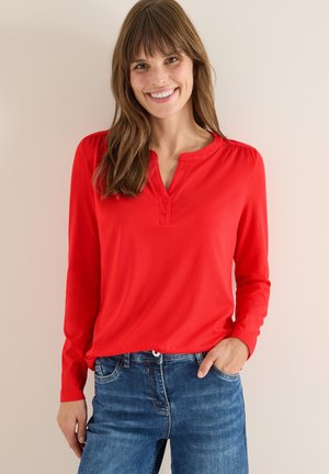 Top rosso a maniche lunghe con scollatura a Henley con bottoni. Tessuto morbido e vestibilità comoda. Abbinato a jeans in denim blu. Design semplice e informale.