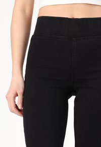 Sorte høye leggings i svart med en glatt tekstur, med bred midje og uten synlig maskinvare eller mønstre. Designet for elastisitet og komfort.