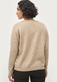 Beige gebreide trui met een ontspannen pasvorm, lange mouwen, ronde hals en geribbelde manchetten. Getextureerde, zachte stof in een effen kleur.