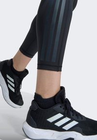Black athletic shoes with three white stripes, paired with black leggings featuring dark grey vertical stripes. Textured materials and snug fit.