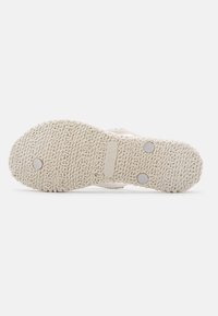 Sole in gomma beige chiaro con grip testurizzato, caratterizzata da indentazioni circolari e borchie metalliche. Dettagli del marchio e della taglia impressi visibili.