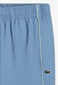 Ανδρικό ανοιχτό μπλε σορτς με υφή, ελαστική μέση και αντίθετη κίτρινη πλαϊνή ρίγα. Διαθέτει το λογότυπο κροκόδειλου της Lacoste.