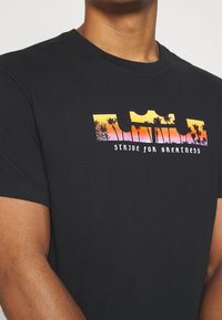 Camiseta negra de algodón con un gráfico colorido de palmeras y un atardecer, junto al texto "ESFUÉRZATE POR LA GRANDEZA". Mangas cortas.