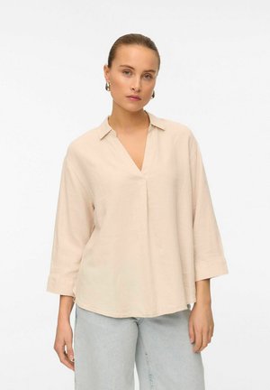 Chemise en lin beige à col en V, à manches longues et à coupe décontractée, avec une texture subtile et des fentes sur les côtés à l'ourlet.