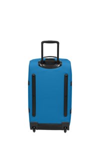 Valigia rigida di colore blu solido con manico nero retrattile, quattro ruote, dettagli neri alla base e strisce protettive lungo i lati.