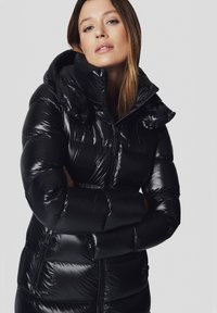 Czarna puchowa kurtka o błyszczącej powierzchni, z kapturem, zapinana na zamek z przodu i elastycznymi mankietami. Zawiera pikowane sekcje oraz dwie boczne kieszenie.