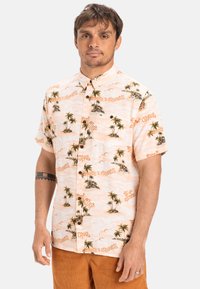 Kortey shirt in licht perzik stof met een tropisch palmbomen- en eilandpatroon, met knopen en een zak op de linker borst.