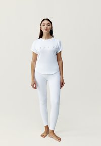 Witte sport T-shirt met opgerolde mouwen en een subtiele voorkant ontwerp, gecombineerd met hoge taille witte leggings, beide gemaakt van een gladde, rekbare stof.