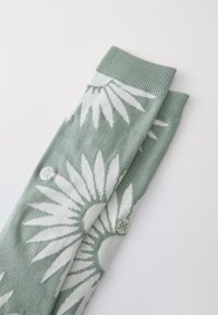 Calzini lavorati a maglia in morbido verde e bianco con un motivo a raggiera, dotati di polsini a costine e accenti circolari ricamati.