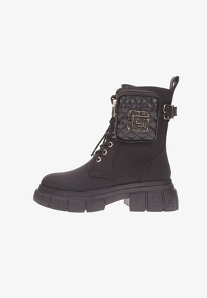 Stivaletto nero con suola piatta spessa, lacci anteriori e tasca trapuntata con dettagli del logo. Realizzato in materiale sintetico testurizzato.