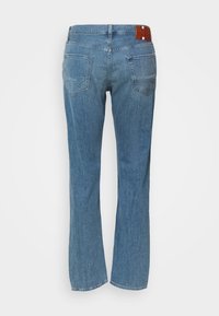 Jeans de mezclilla azul claro con diseño de pierna acampanada, cinco bolsillos y una parche de cuero marrón con el logo en la cintura trasera.
