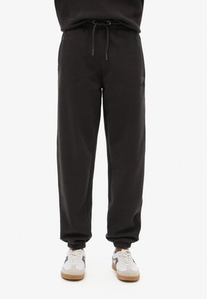 Pantalons de survêtement noirs avec une taille à cordon, des poignets élastiques et des poches latérales. Fabriqués en tissu doux avec une texture lisse.