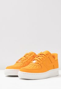 Une paire de baskets basses orange vif avec des semelles et des lacets blancs, présentée sur un fond blanc uni.