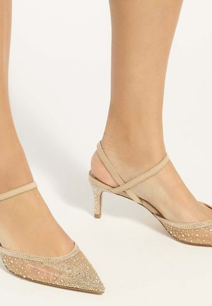 Beige spitze High Heels mit Knöchelriemen, verziert mit kleinen funkelnden Strasssteinen auf Mesh-Stoff, getragen an nackten Füßen.