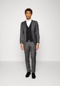 Grau kariertes Anzug mit einer schwarzen Weste, weißem Hemd und schwarzen Schuhen. Slim-Fit-Design mit taillierten Details und glatten Texturen.