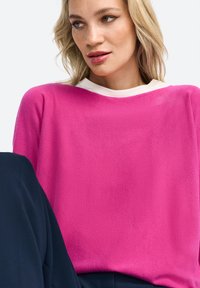 Roze trui met een gestructureerde afwerking en een witte ronde hals. De pasvorm is ontspannen en het heeft een zachte, lichte stof.