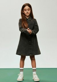 Vestido camisa de mezclilla oscura con cuello puntiagudo, botones frontales y mangas largas, combinado con zapatillas blancas y calcetines a rayas.