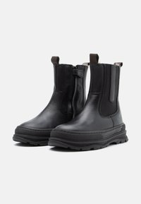 Bottines noires en cuir avec des panneaux élastiques sur les côtés, une semelle en caoutchouc épaisse et une fermeture éclair sur le côté. Design minimaliste avec des textures contrastées.