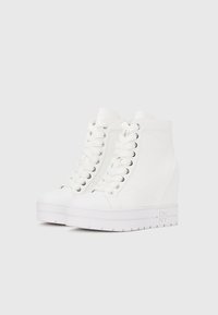 Adidași albi înalți, cu partea superioară texturată, vârf rotund, șireturi plate și toc cu pană. Prezintă un logo în relief pe lateral și tălpic gros.