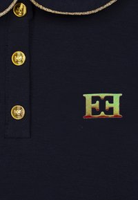 Polo navy con bottoni dorati, caratterizzato da un logo oro e rosso. La trama appare liscia, con un colletto dorato a contrasto.
