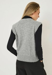 Gray, sleeveless knit sweater with ribbed hem, made from soft material. Features minimal detailing at the back and a relaxed fit.