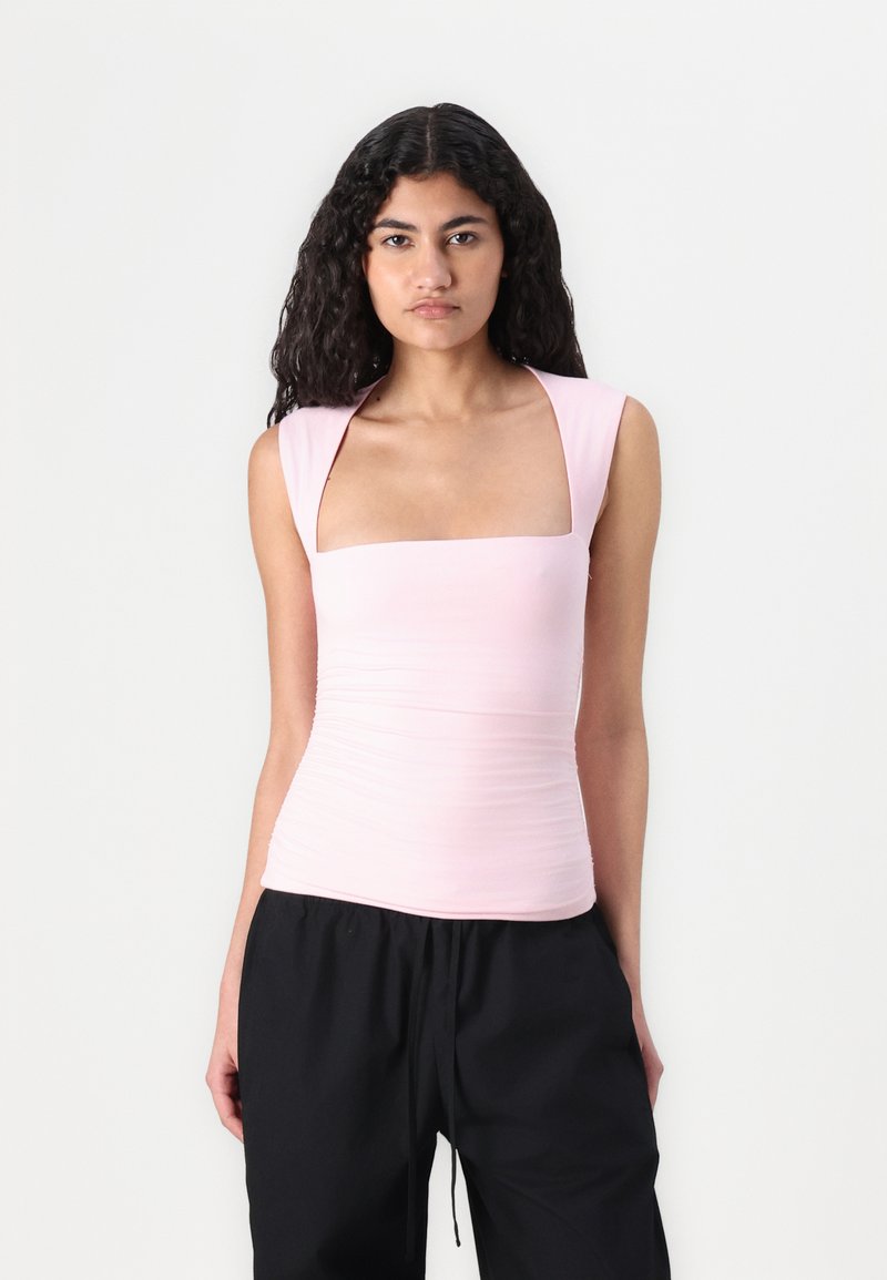 Top sin mangas ajustado de color rosa claro con escote cuadrado y tirantes anchos, que presenta detalle fruncido a lo largo de los costados.