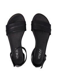 Een paar zwarte leren sandalen met open tenen, brede banden en enkelgespen, met het label "Venezia" op de gevoerde zool.