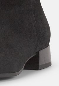 Černé semišové kotníkové boty s zaoblenou špičkou a nízkým texturovaným blokovým podpatkem. Materiál má měkký, matný povrch.