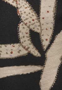 Strickstoff mit schwarzem Hintergrund, auf dem leichte beige abstrakte Formen und gepunktete Muster zu sehen sind, akzentuiert mit rötlich-braunen Details.