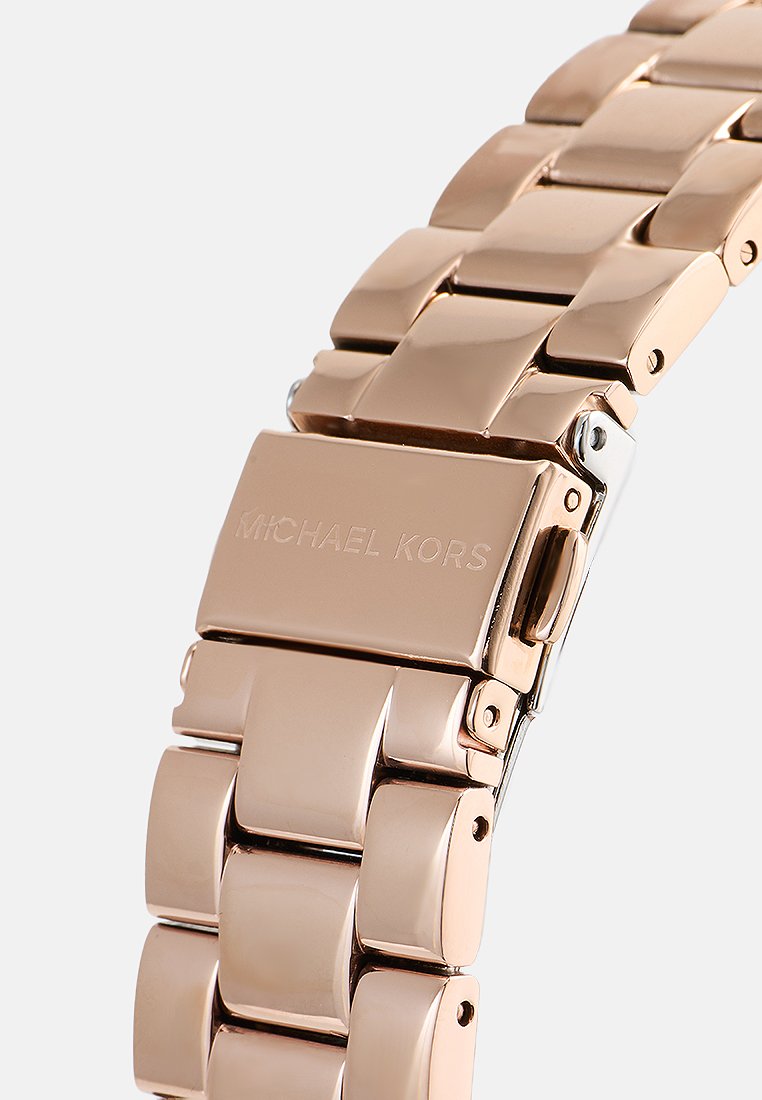 Bracelet de montre en métal rose doré avec des maillons polis et une marque gravée. Il possède un fermoir à rabat et des bords lisses et arrondis.