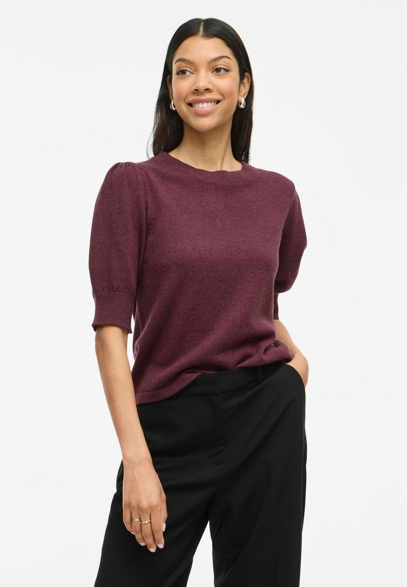 Pull bordeaux à manches courtes avec un tissu texturé, col rond et manches bouffantes, associé à un pantalon noir.