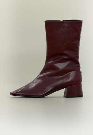 Bottine en cuir bordeaux à bout pointu, tige souple et plissée et talon bloc épais, présentée de profil sur un fond uni.