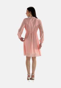 Abito rosa a strati con maniche lunghe, vita stretta e una silhouette morbida e fluida. Il tessuto è leggero e semitrasparente.