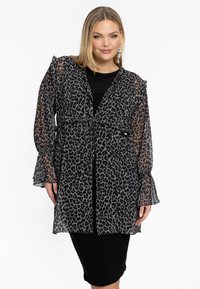Leopardskin doorzichtig kimono met zwarte accenten, featuring lange rimpels mouwen, een strik taille, en een gelaagd ontwerp, gedragen over een zwarte jurk.