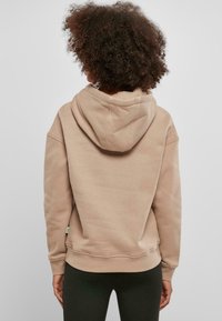 Beige hettegenser med en avslappet passform, ribbede ermer og hem. Tekstilet har en myk tekstur, enkel design og synlige sømdetaljer.
