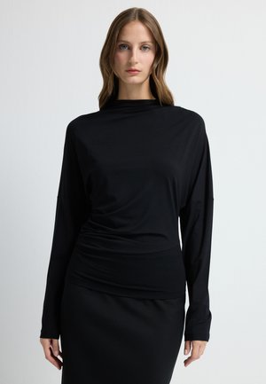 Zwarte langemouwtop met een relaxed fit, met een gedrapeerd ontwerp en een zachte, gladde textuur. Gecombineerd met een bijpassende zwarte rok.