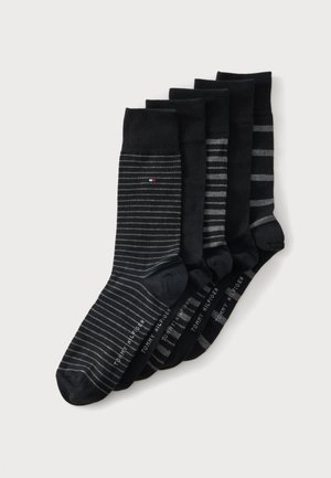 Cinq paires de chaussettes noires avec différents motifs de rayures grises, disposées en chevauchement, chacune avec le texte "Tommy Hilfiger" près des orteils.