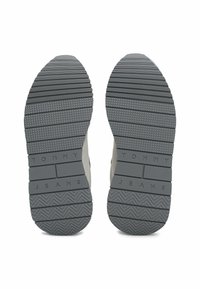 Las suelas de los sneakers grises tienen un diseño texturizado con surcos horizontales y diagonales. "TOMMY JEANS" está grabado en la superficie de goma.