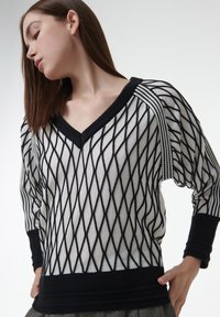 Schwarzer und weißer gestrickter Pullover mit einem Rautenmuster, V-Ausschnitt und langen Ärmeln mit kontrastierenden Rippenbündchen und Saum.