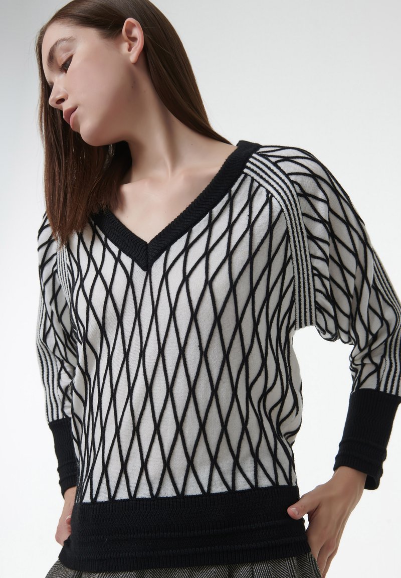Schwarzer und weißer gestrickter Pullover mit einem Rautenmuster, V-Ausschnitt und langen Ärmeln mit kontrastierenden Rippenbündchen und Saum.
