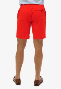 Pantalones cortos rojos brillantes con una cinturilla elástica, bolsillos laterales y un bolsillo trasero con cremallera. Fabricados en un tejido suave y ligero.