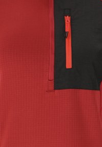 Kurzarmpulli mit einem strukturierten roten Oberteil, einem einfarbigen schwarzen Einsatz und einer orangefarbenen Reißverschlusstasche auf der Brust.