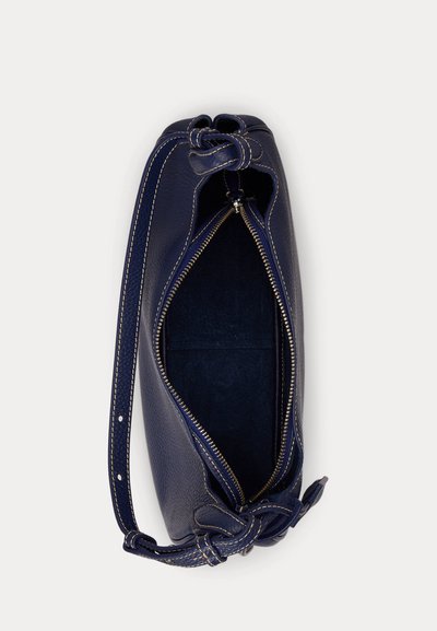 Piccola borsa a mano in pelle blu navy con cerniera superiore parzialmente aperta e tracolla annodata su sfondo semplice.